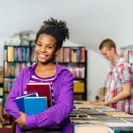 Estudante sorrindo com livros em uma biblioteca